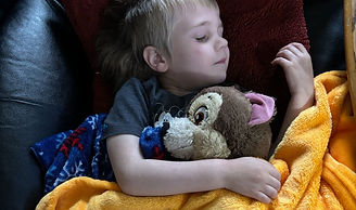 a child sleeping with an orange blanket and holding a teddy bear