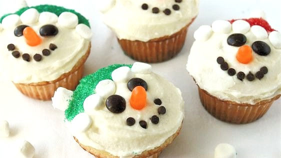 kid friendly snowman cupcakes decorated with marshmallows, chocolate chips and assorted fruit and chocolate candies