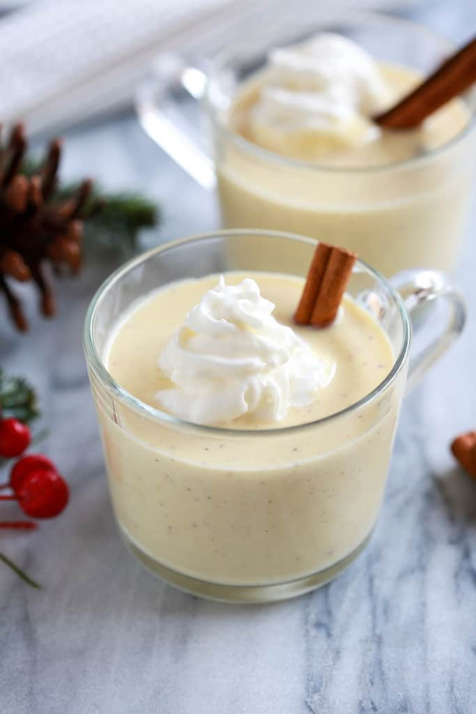 made from scratch eggnog served in glass mugs topped with a dollop of whipped cream and garnished with a cinnamon stick