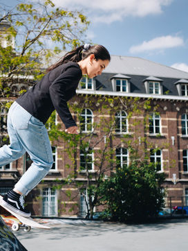 Eine Skaterin mit Pferdeschwanz, stürzt sich auf dem Board von einem Hindernis.