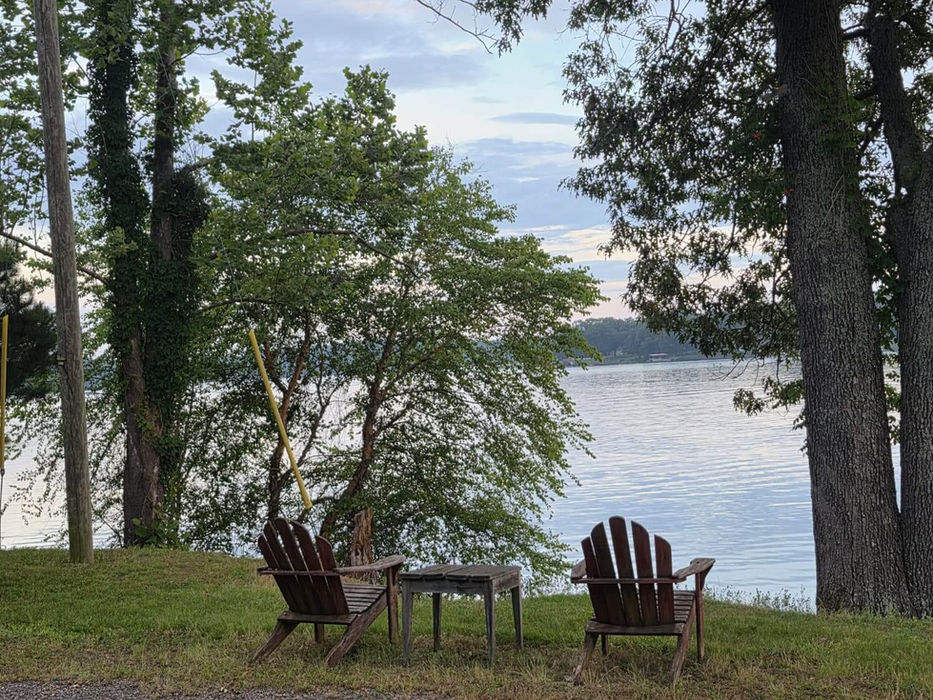 Two wooden chairs facing a calm lake at sunset.