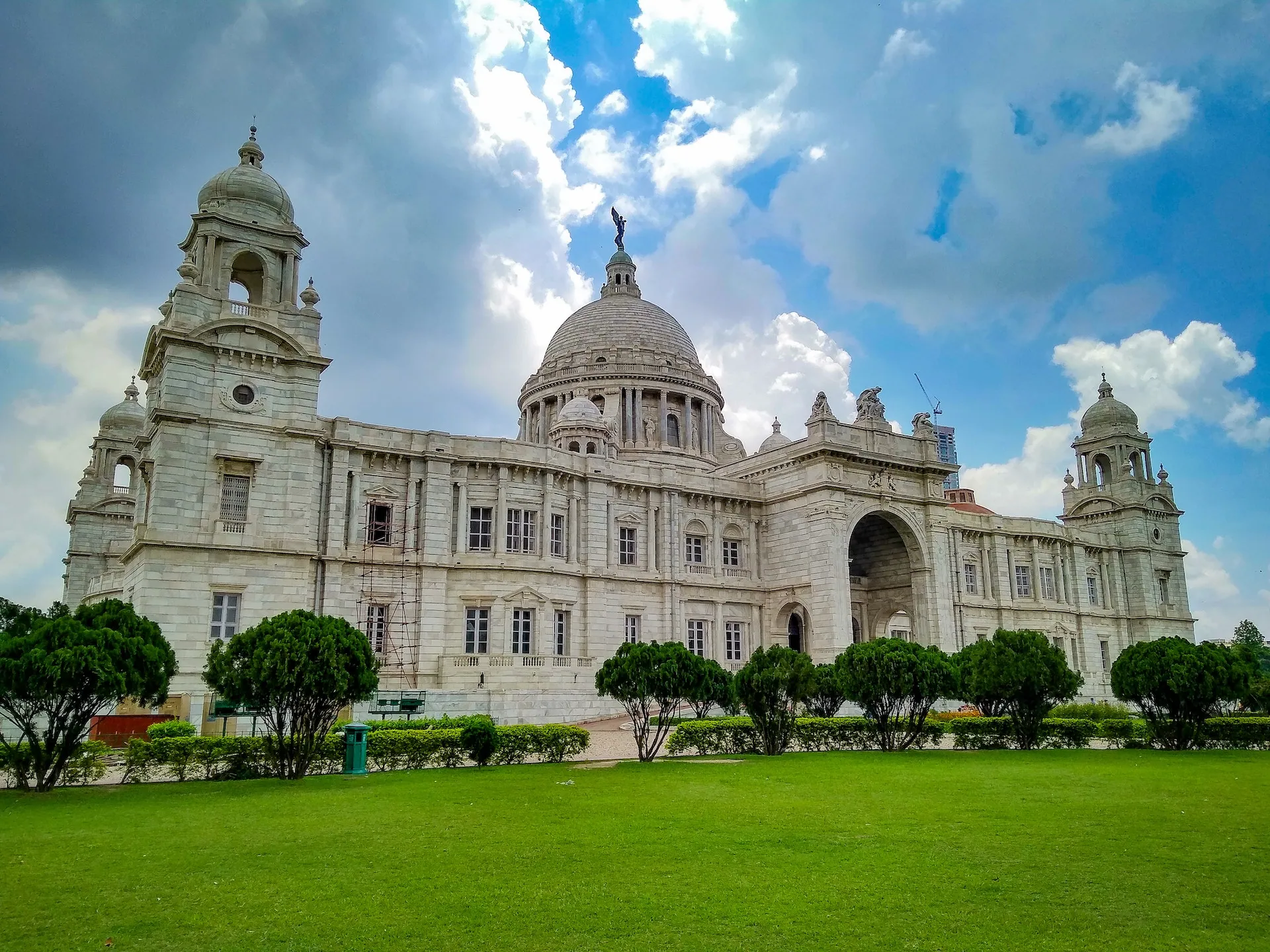 A majestic white marble building with a large central dome and several smaller domes, surrounded by lush green gardens and a reflecting pool.