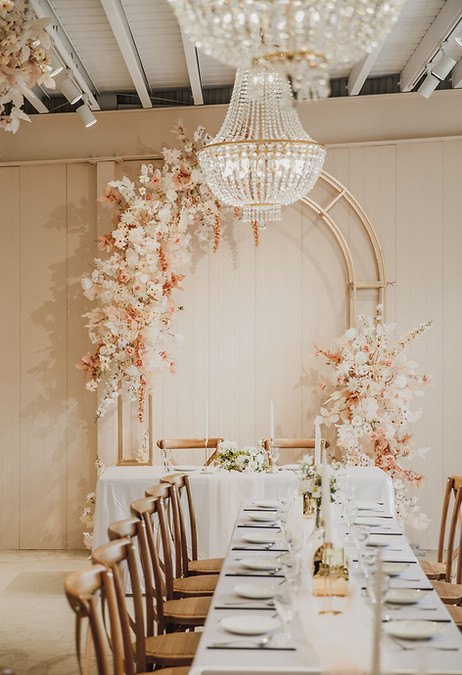 桃園扶日 Wedding 室內婚宴場地布置,中央擺放奶茶色花拱門與水晶吊燈,木質桌椅與白色桌巾圓桌營造溫馨典雅的婚禮氛圍