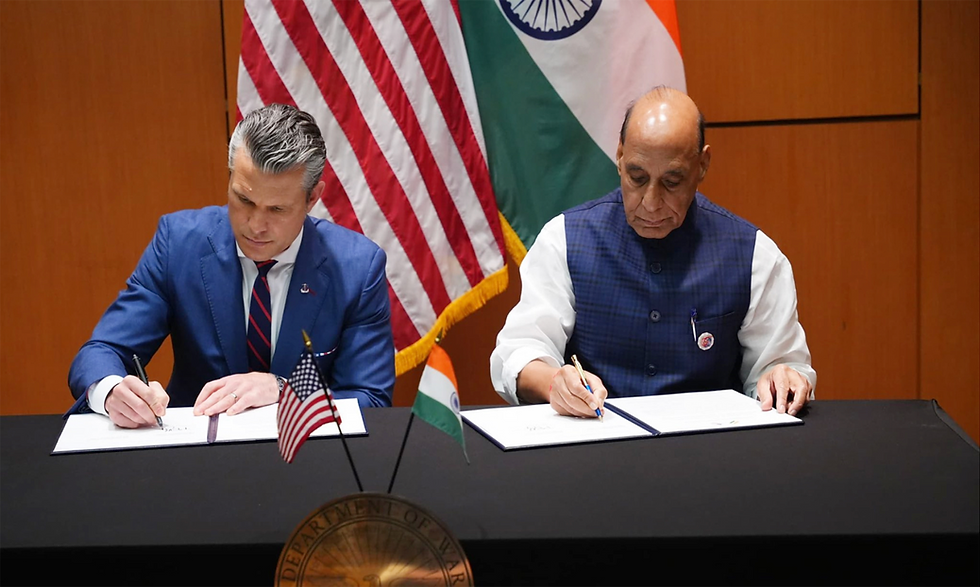 Two men in formal attire sign documents at a table. U.S. and Indian flags are visible in the background, setting a diplomatic tone.