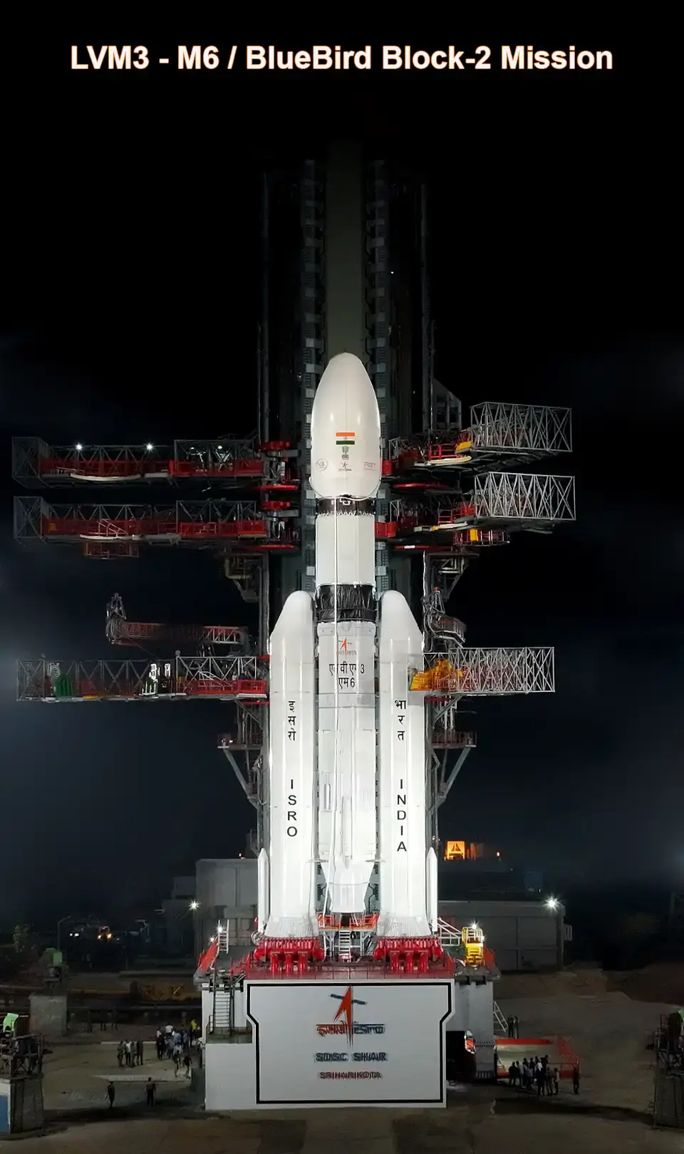 Rocket on launch pad at night, labeled ISRO and INDIA. Text above reads "LVM3 - M6 / BlueBird Block-2 Mission." Lights illuminate scene.