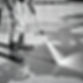 Black and white close-up image of a man pressure washing a concrete driveway or street. Th