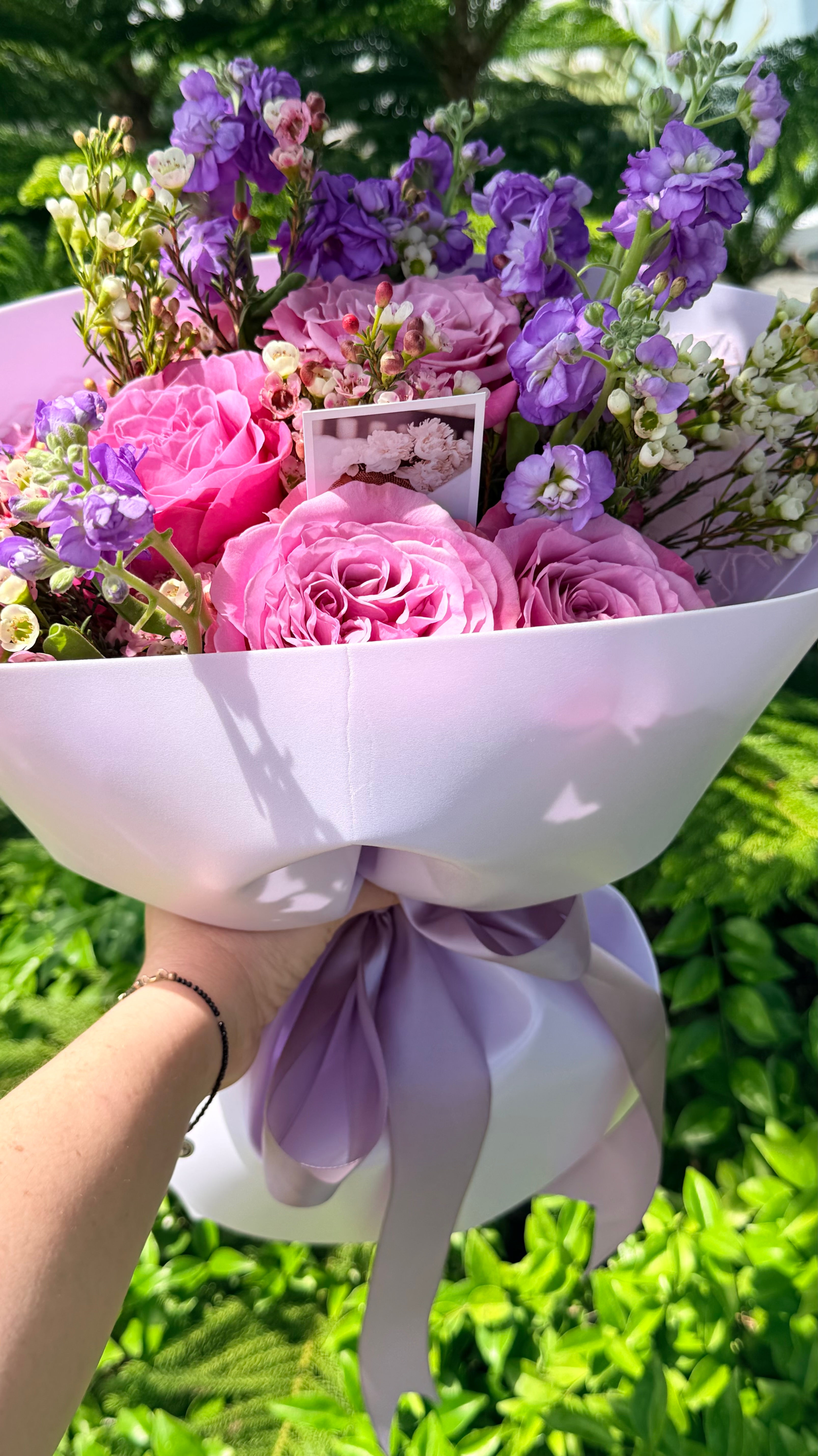 Lavender Blush™ bouquet featuring premium pink garden roses, lavender stock, wax flowers, and seasonal flowers wrapped in blu