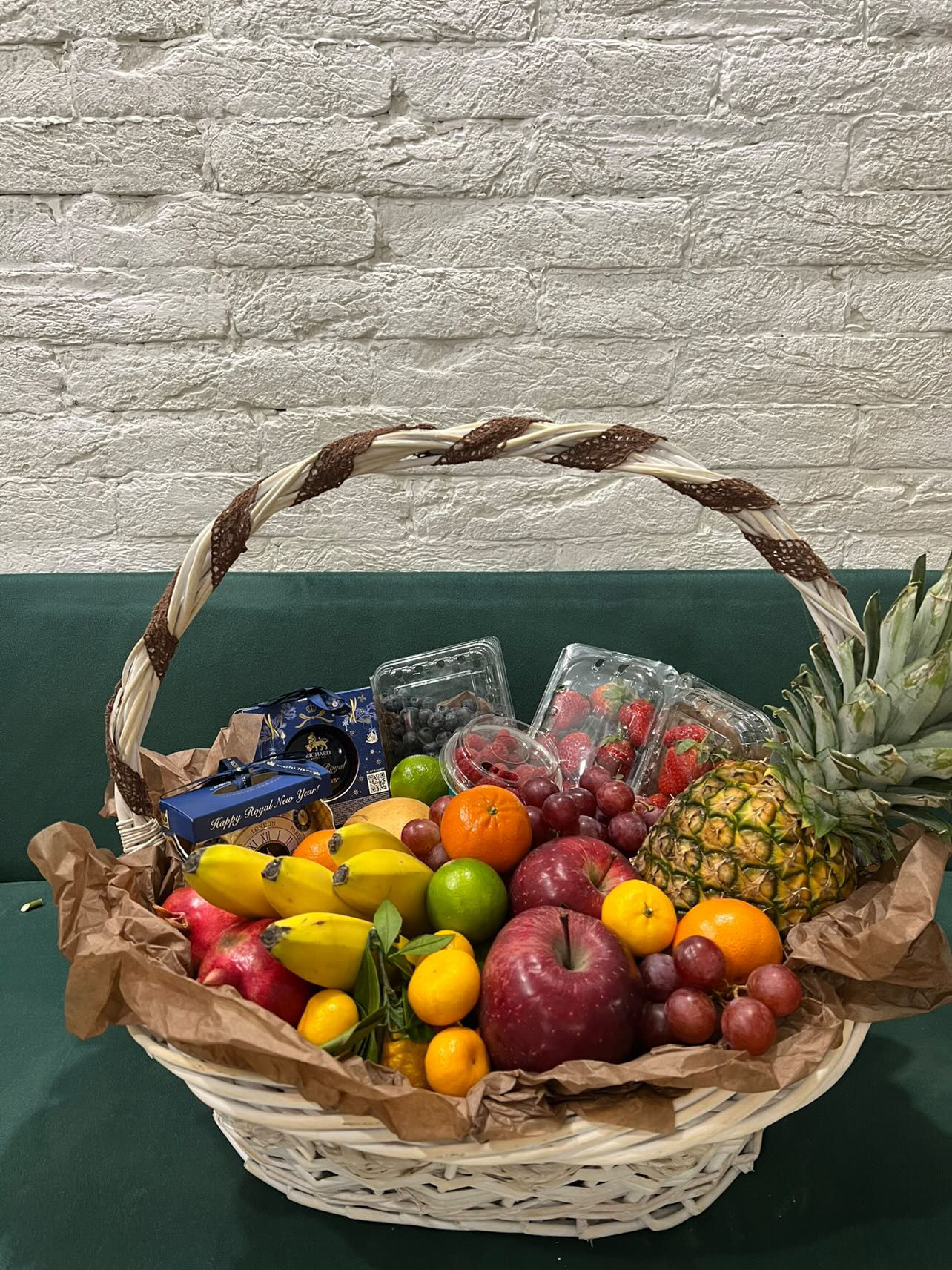 Luxury fruit basket with pineapple, apples, grapes, berries, and holiday packaging.