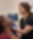 A nurse wearing a black uniform examines a patient's face, marked with white outlines, assisted by a digital monitor in a cli