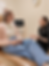 A patient sits on an exam table holding a mug while talking with a healthcare provider, who is also holding a mug, in a medic