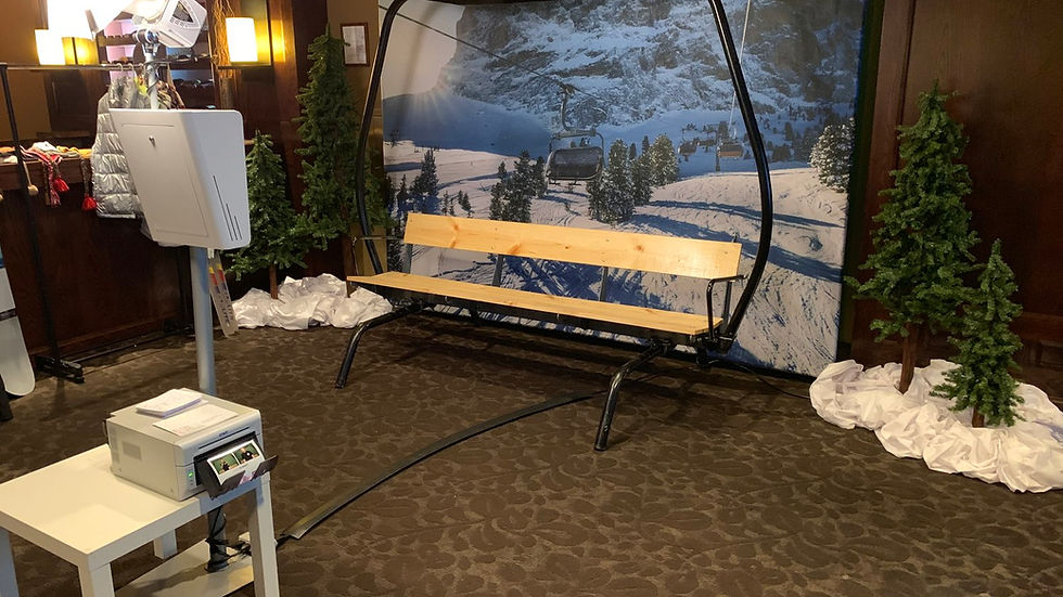 Our Ski Lift Photo Set, posed in front of a Photo Booth with a printer. The Ski Lift is wooden with a themed ski lift backdrop behind it, perfect for corporate or social events.