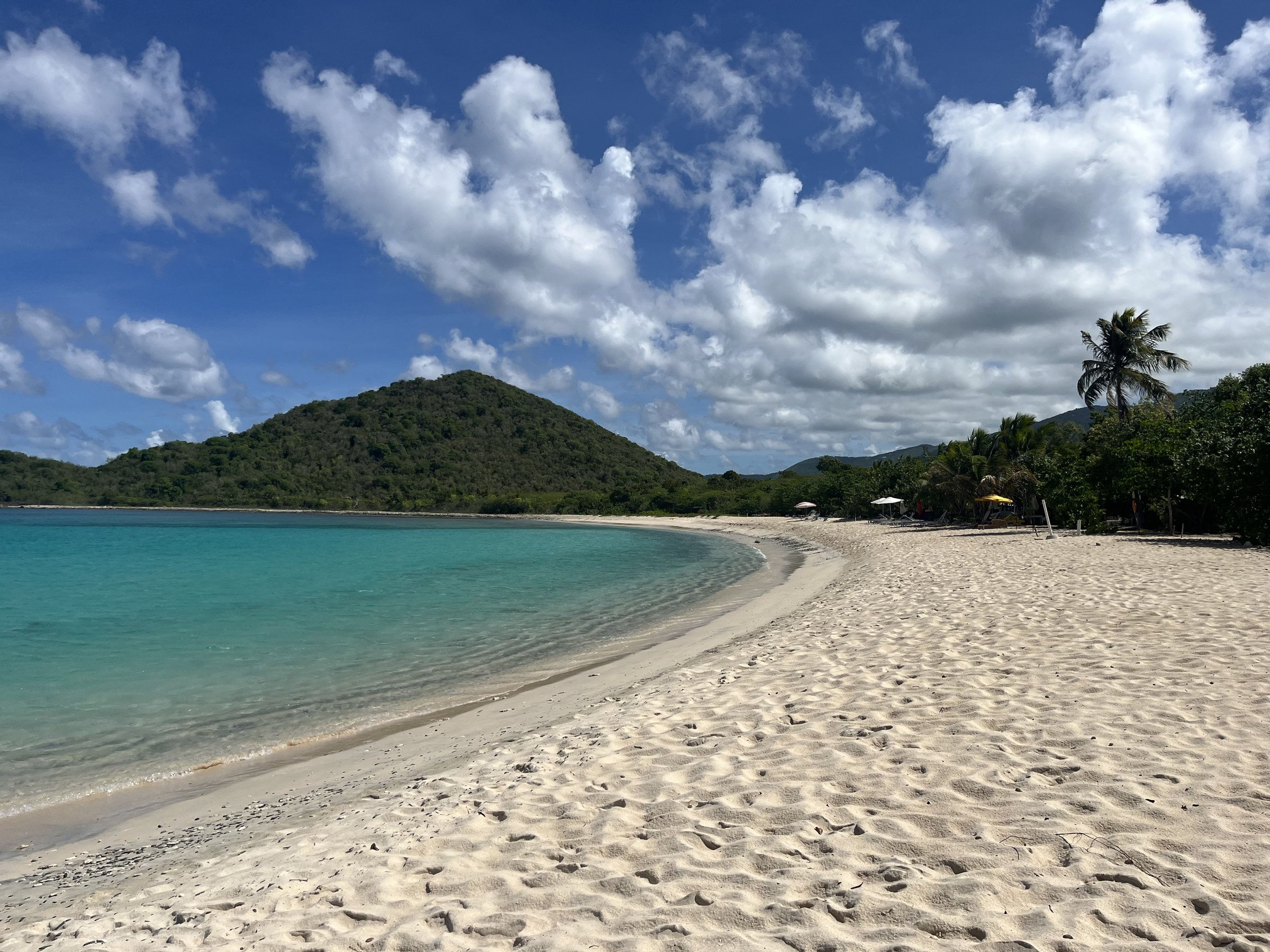 Empty white-sand secret beach curving to a green hill on a private Tortola SUV day