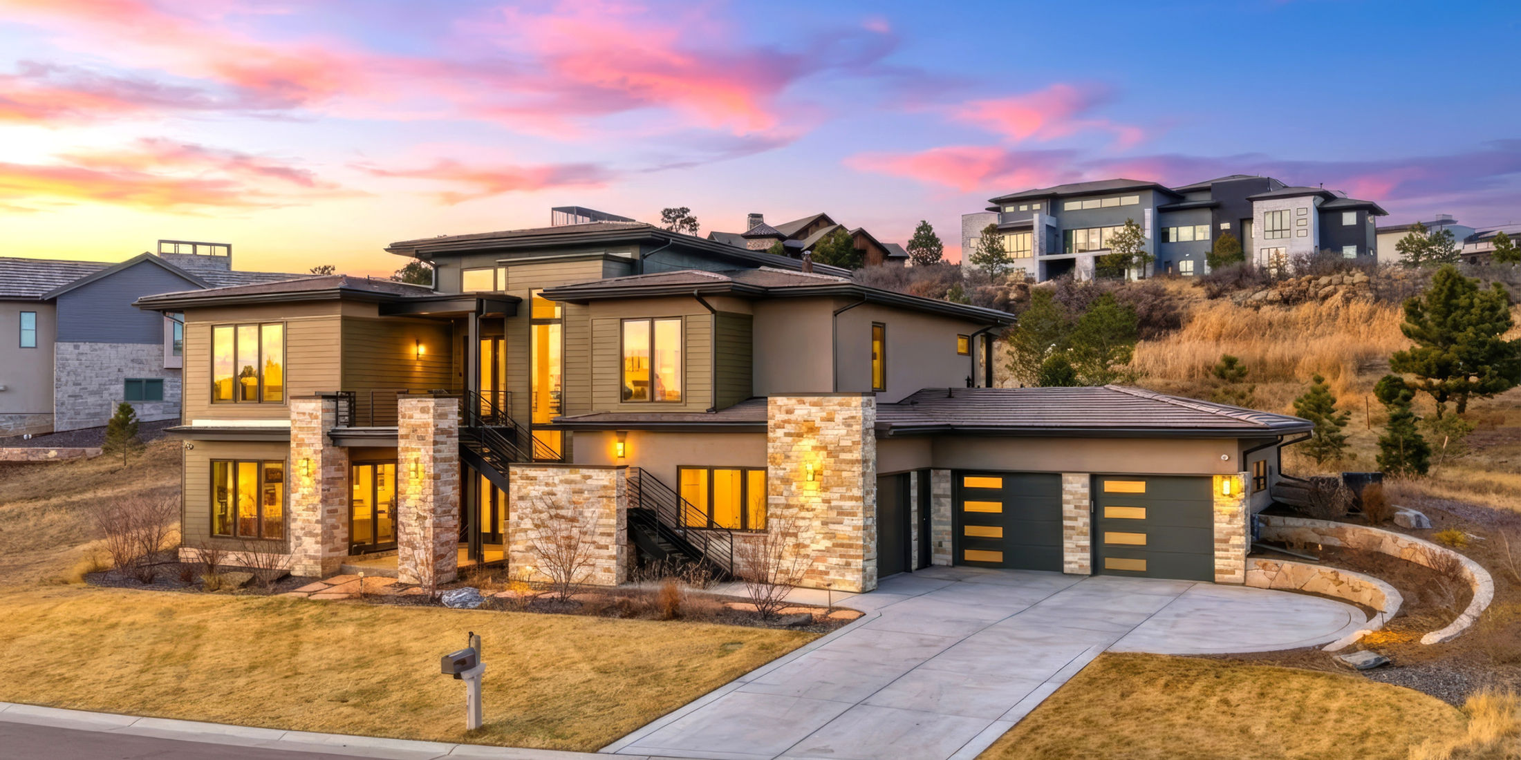 Contemporary home with stone columns and lit windows at dusk
