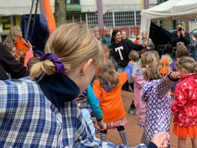 Kinderen dansen buiten, met een vrouw in een 'T' shirt. Tamar Riani