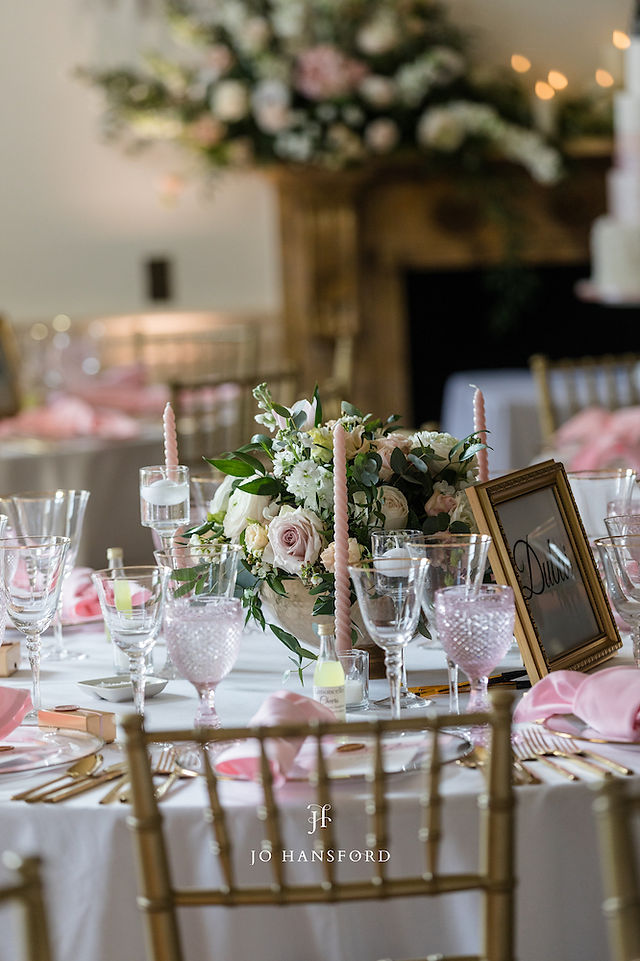 Low table florals in a gold bowl surround with blush pink candles, floating candles and votives to compliment the gold cutlery and blush pink glasses ready for the wedding breakfast in the ballroom of North Cadbury Court. 