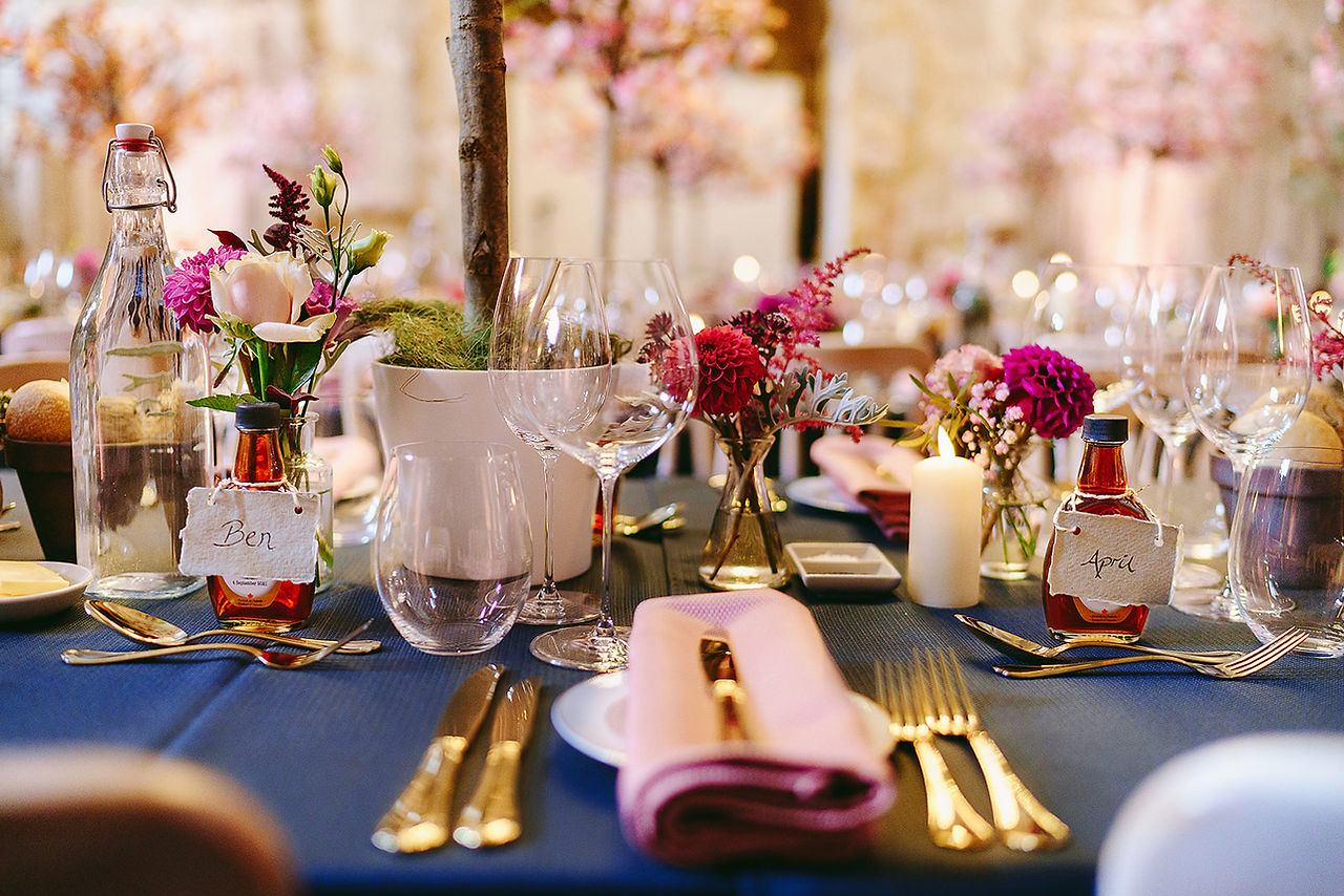 wedding tables adorned with gold cutlery, gold  and clear vases  full of rich coloured flowers with LED candles 