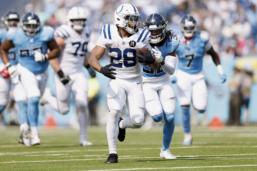 Football players in white and blue uniforms run on a green field. One player holds a ball, closely pursued by opponents.