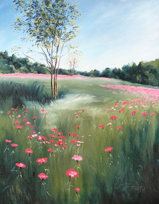 A landscape featuring red & pink poppies vanishing into the distance of a large green field with sapling trees in front of a wooded dark green background under a gradated blue sky