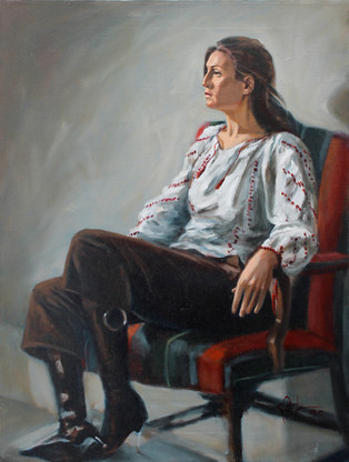 A lovely young woman wearing Romanian clothing and stiletto boots featuring a large ring sits on a multi-striped arm chair elevated on a platform