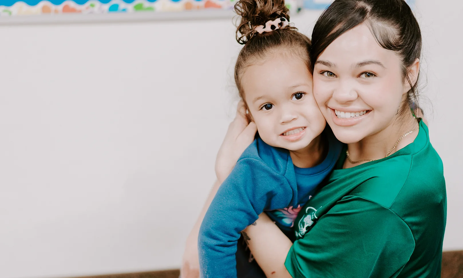 Wellspring Academy teacher and child share a close, smiling embrace indoors.