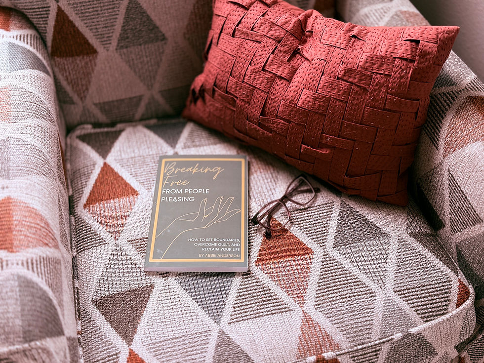Book titled "Breaking Free from People Pleasing," glasses on a patterned chair with a red cushion. Calm setting, warm colors.