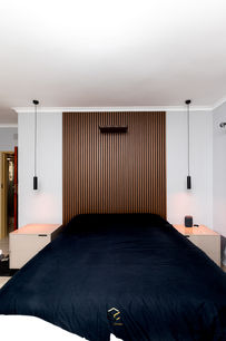 Master bedroom interior design featuring a wooden slatted headboard wall, pendant lights, and two matching bedside pedestals.