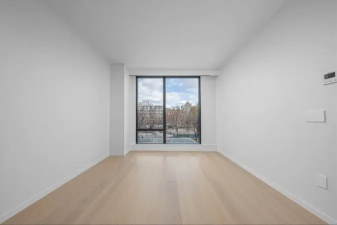 Bright bedroom with large window and white oak flooring in a new LIC two-bedroom apartment