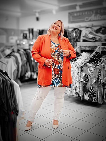 Femme grande taille souriante portant un blazer orange avec tunique colorée et pantalon clair, look élégant disponible à Yverdon.