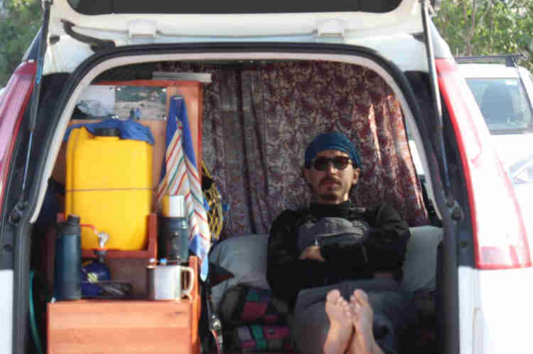 Oleh Nikita Smelyanskiy laying in the back of his van on a blanket with storage containers next to him