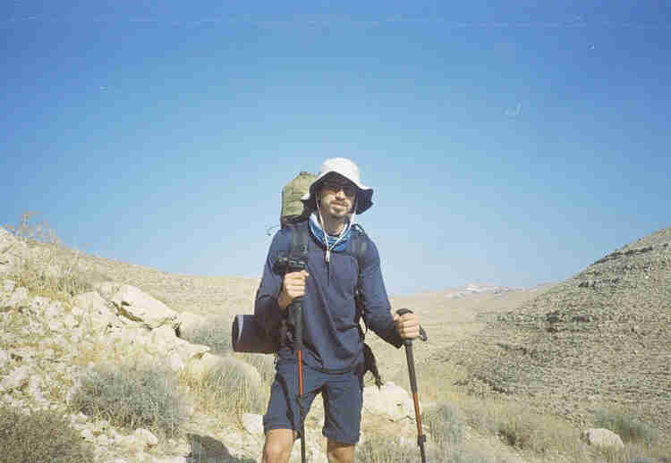 Oleh Nikita Smelyanskiy holding walking sticks in each hand, wearing a white hat, and large backpack outside