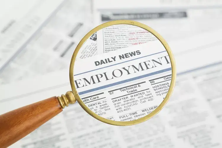 Magnifying glass over a newspaper job listings page, highlighting Daily News Employment in bold black text on white background.