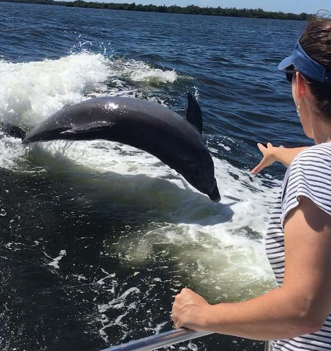 A woman watching a dolphin jump out of the water beside a boat