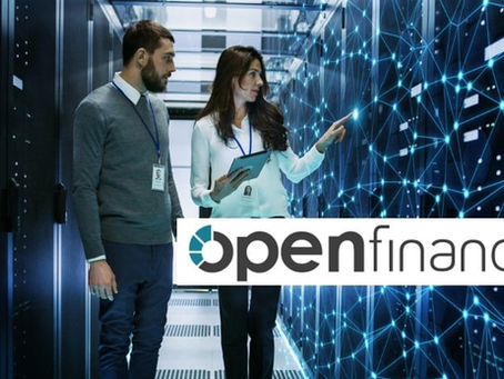Dois profissionais em sala de servidores; mulher aponta para painel digital azul com logotipo openfinance.