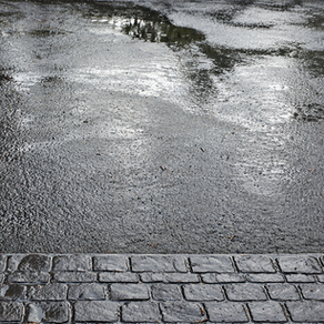 Nasser Asphalt mit Wasserreflexionen und dunklem Kopfsteinpflaster im Vordergrund