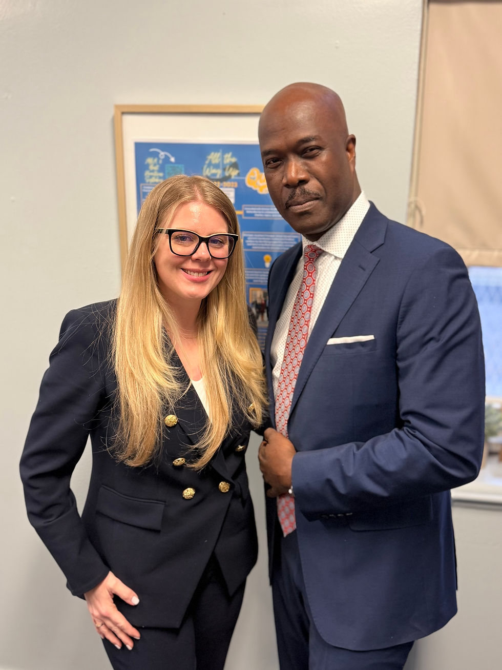 A blonde woman and a man wearing suits and smiling