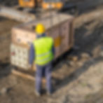A construction worker in hi vis and hard hat guides a diesel generator as it is lowered onto a construction site.
