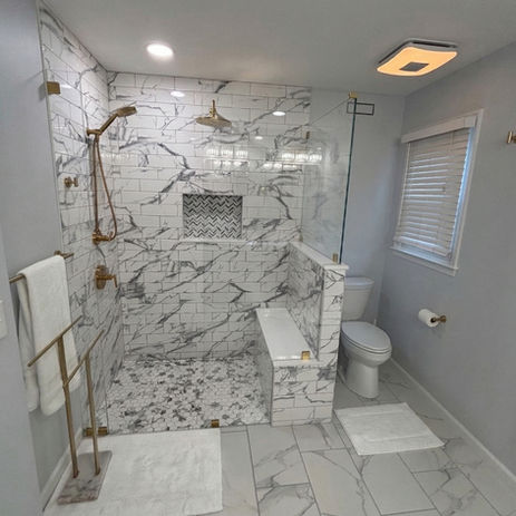 Luxury curbless walk-in shower remodel with marble tile surround, built-in bench, herringbone floor tile, and gold fixtures by Booth Home Impressions in South Jersey