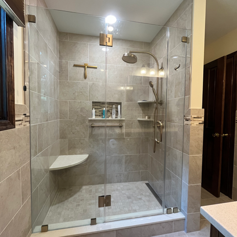 Bathroom remodel with frameless glass shower enclosure, large format gray tile surround, built-in bench, rain shower head, and gold fixtures in South Jersey