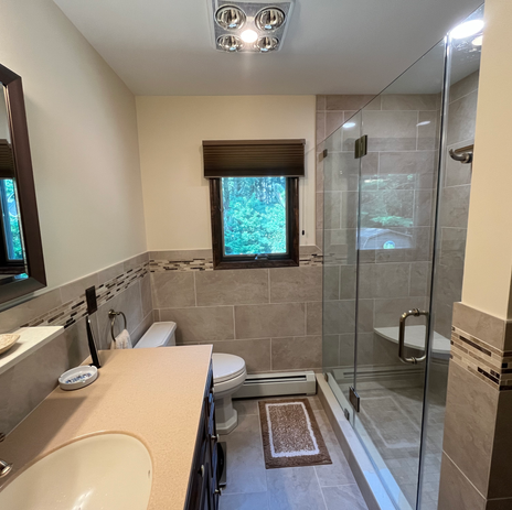 Full bathroom renovation with frameless glass shower, large format gray tile, decorative tile border, single vanity, and vaulted ceiling by Booth Home Impressions in South Jersey