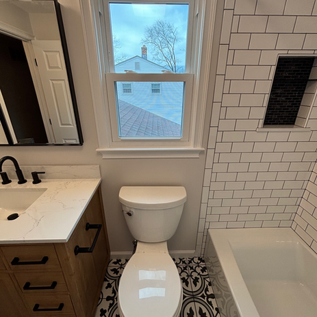 Bathroom remodel with wood tone vanity, white quartz countertop, matte black fixtures, subway tile shower surround, and patterned encaustic floor tile in South Jersey