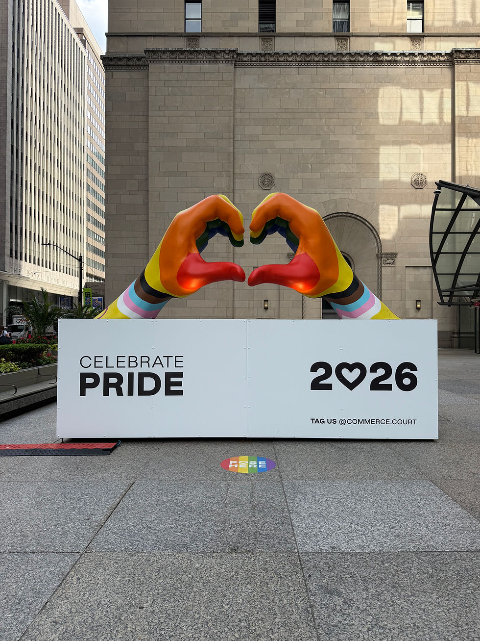 Rainbow hands form a heart above a Celebrate Pride 2026 sign in a city plaza with tall buildings.