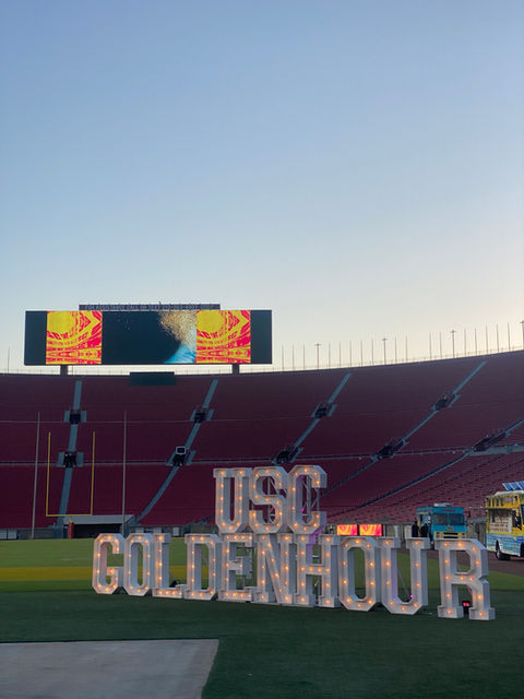 Illuminated 'USC GOLDEN HOUR' Marquee Letters on a stadium field during sunset.