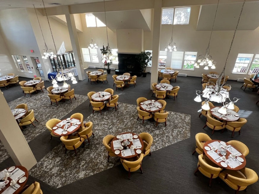 Spacious dining area with round tables, yellow chairs, and patterned carpet flooring.