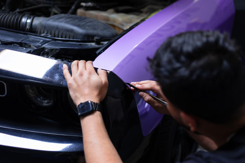 Technician applying black vinyl wrap over purple hood in Temecula, CA