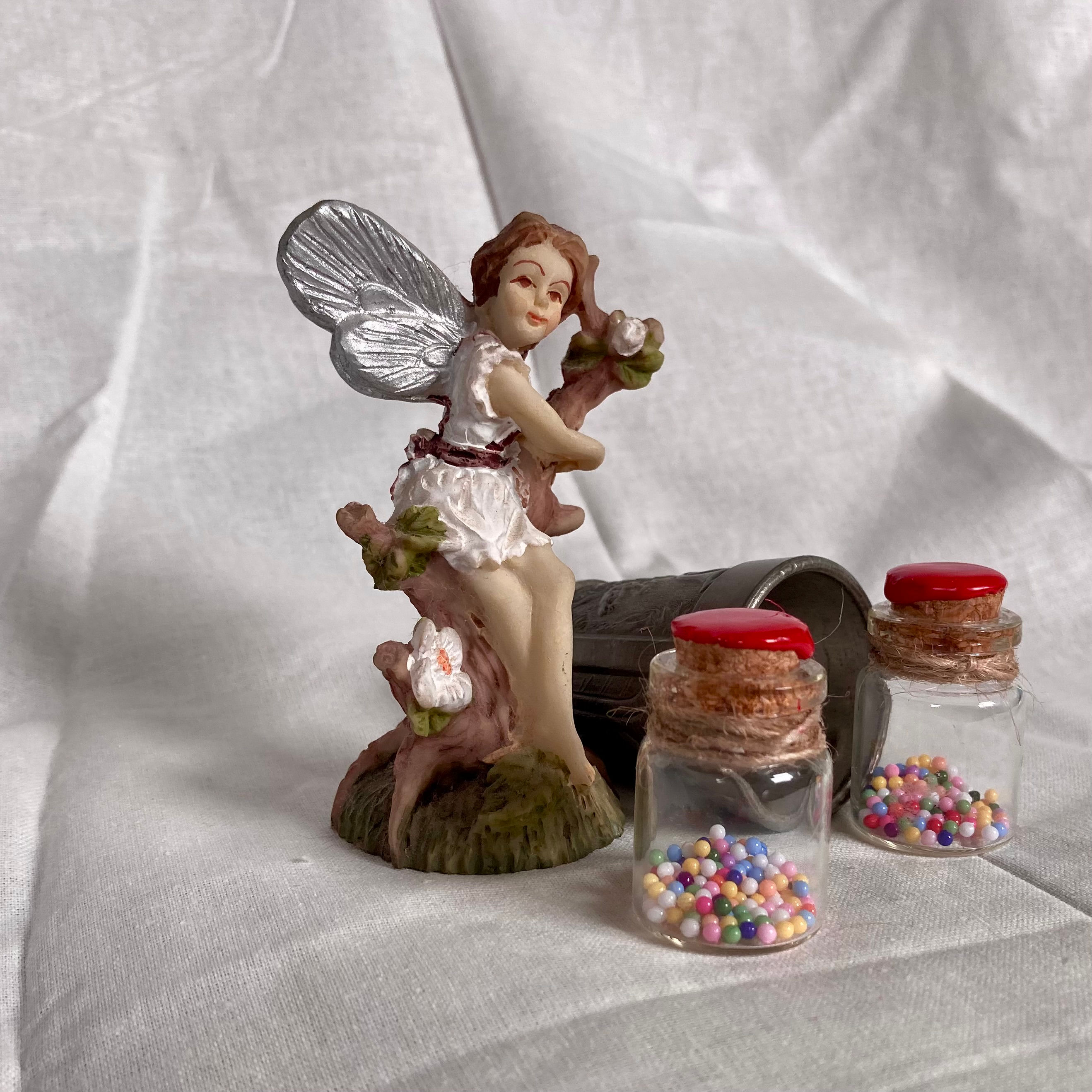 Fairy figurine sitting on branch with two small jars of fairy bubble gum
