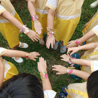 Children show their handmade flower bracelets outdoors.