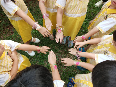 Children show their handmade flower bracelets outdoors.