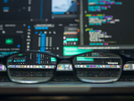 A pair of glasses sits in front of a computer screen. Everything is blurred except what can be seen through the glasses.