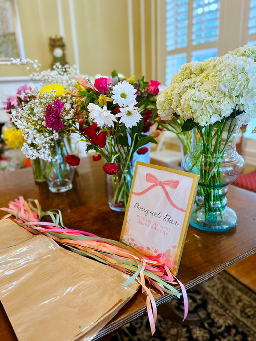Day-of signage for bridal shower. "Bouquet Bar" sign sits with vases of flowers, ribbon, and craft paper.