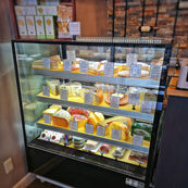 A display fridge showcasing a variety of specialty cheeses, Canadian cheeses and European Cheeses. The fridge is located in a cheese shop. 
